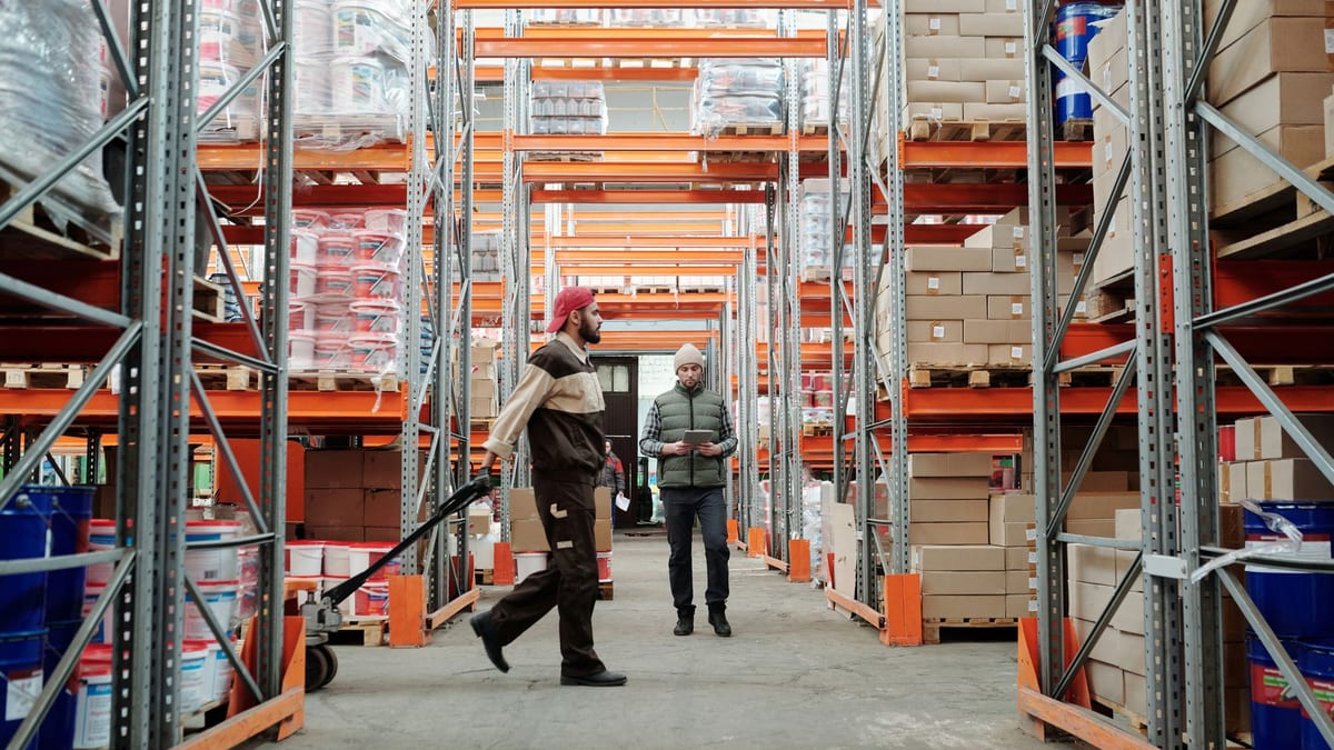Two workers walking down a wide warehouse aisle lined with stocked shelves
