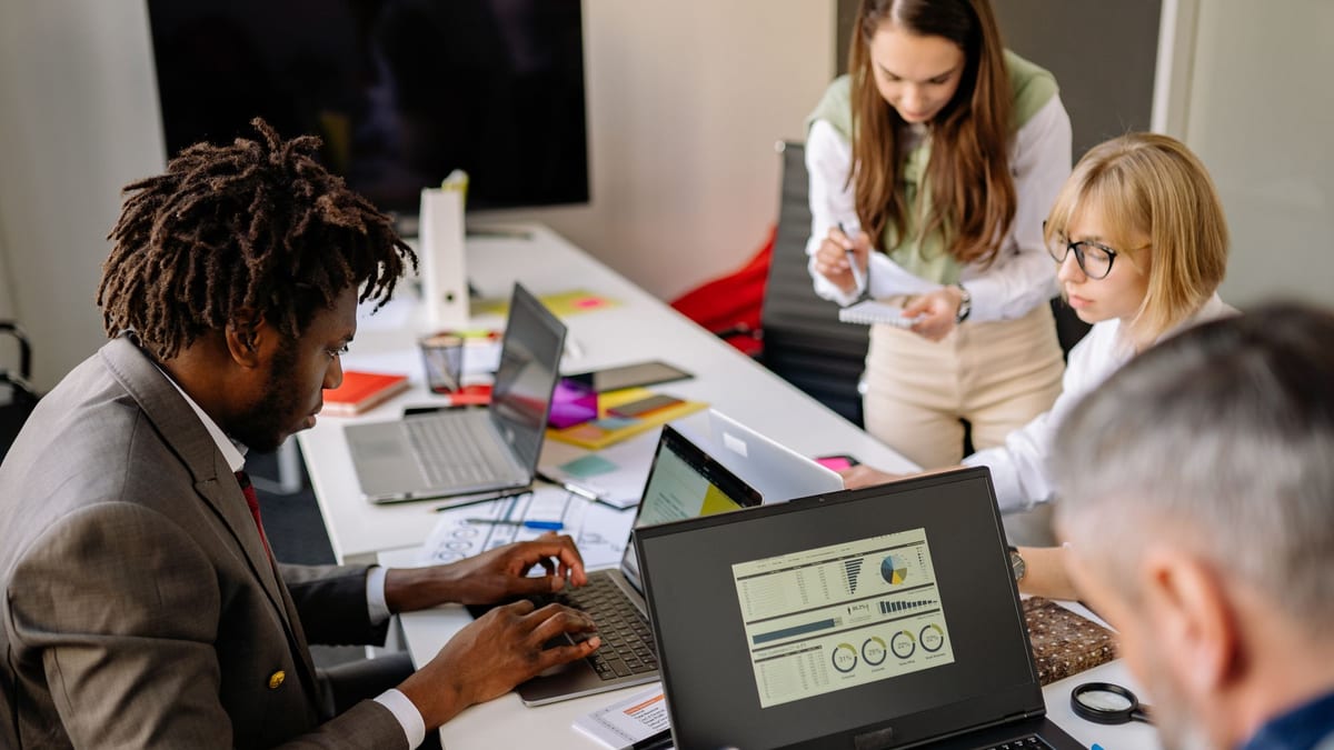 A diverse team working on laptops around a shared office desk, one screen showing a dashboard
