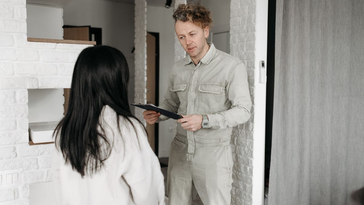 A technician in overalls holding a tablet while talking with a homeowner indoors