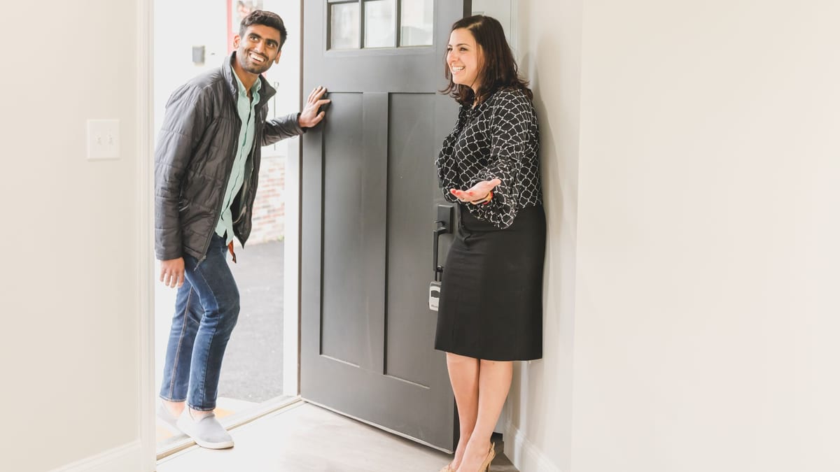 A property agent greeting a visitor at the front door of a home